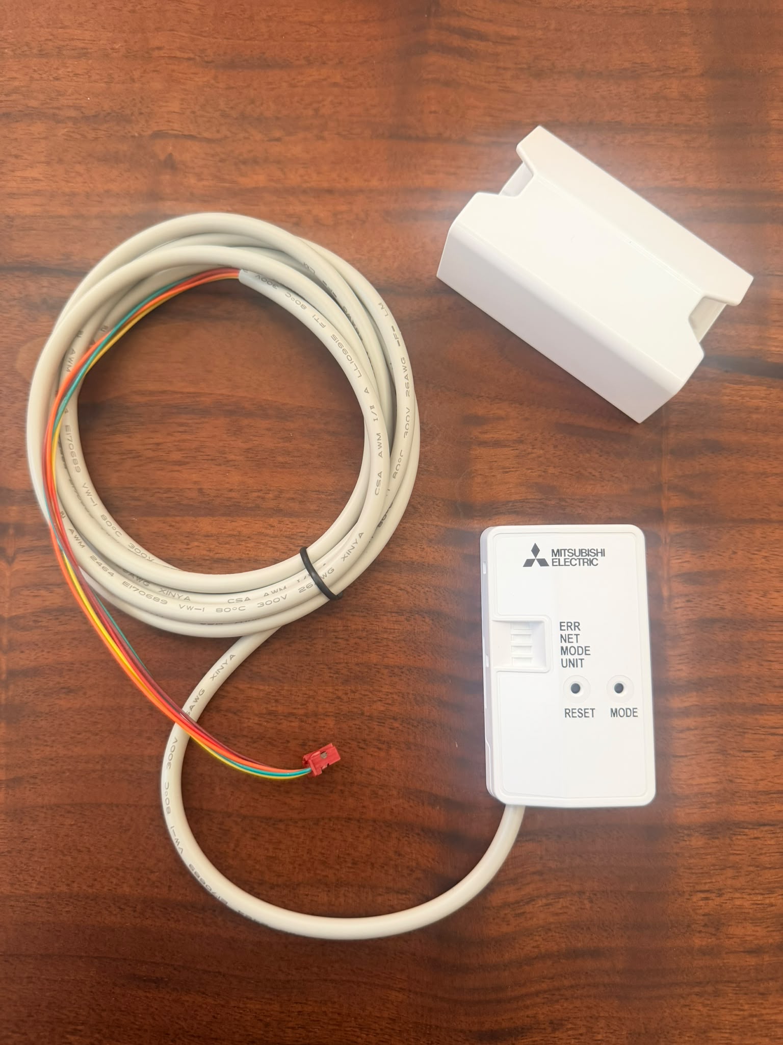 White electronic module and a long coiled cable with colorful wires on a wooden table (Mitsubishi Electric device visible).